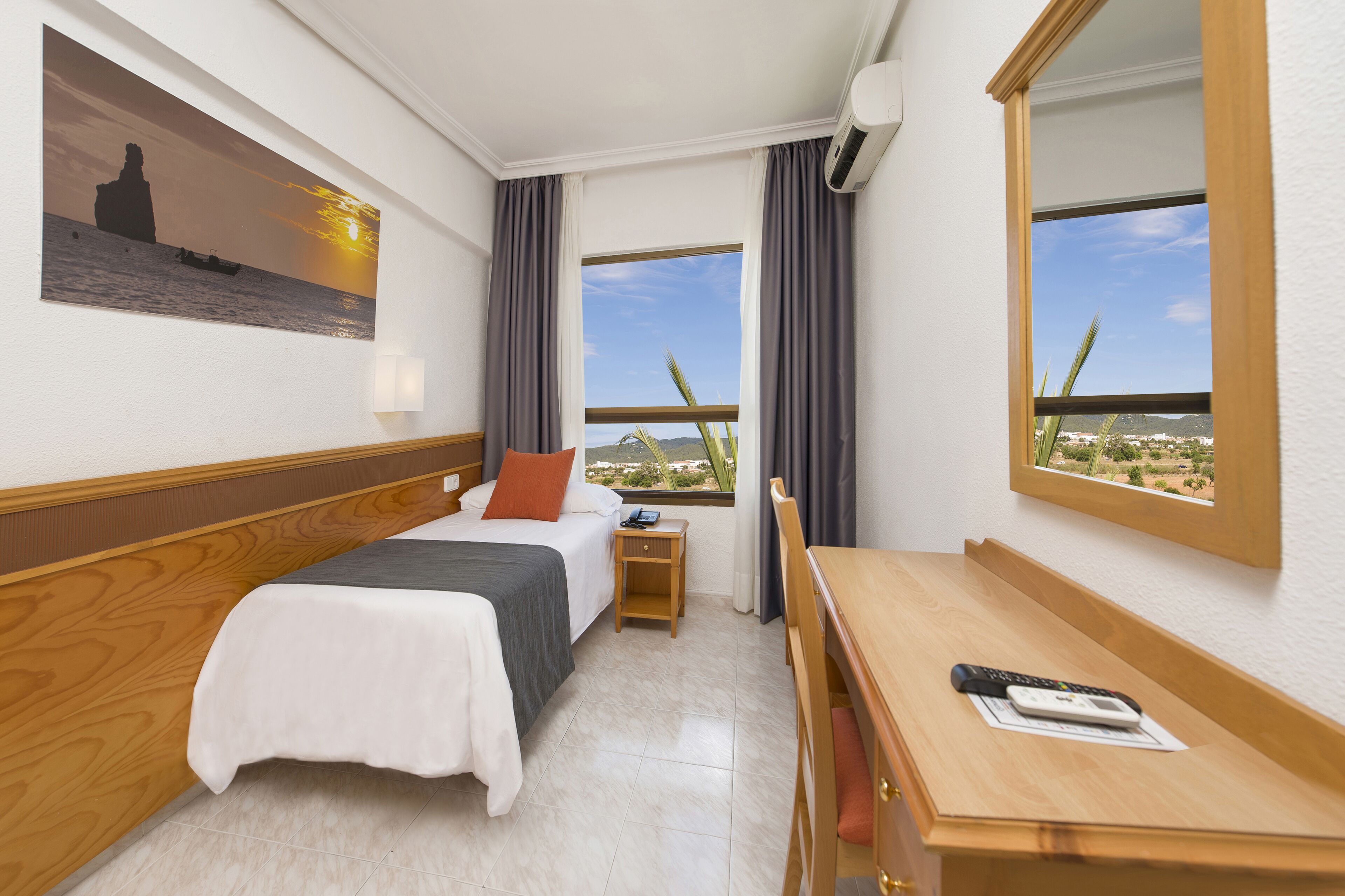 Habitació d'hotel amb llit, taula de nit, escriptori i vista al paisatge desèrtic.