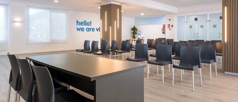A modern conference room with a long table and chairs, a projector, and a 'hello! we are vi' sign on the wall.