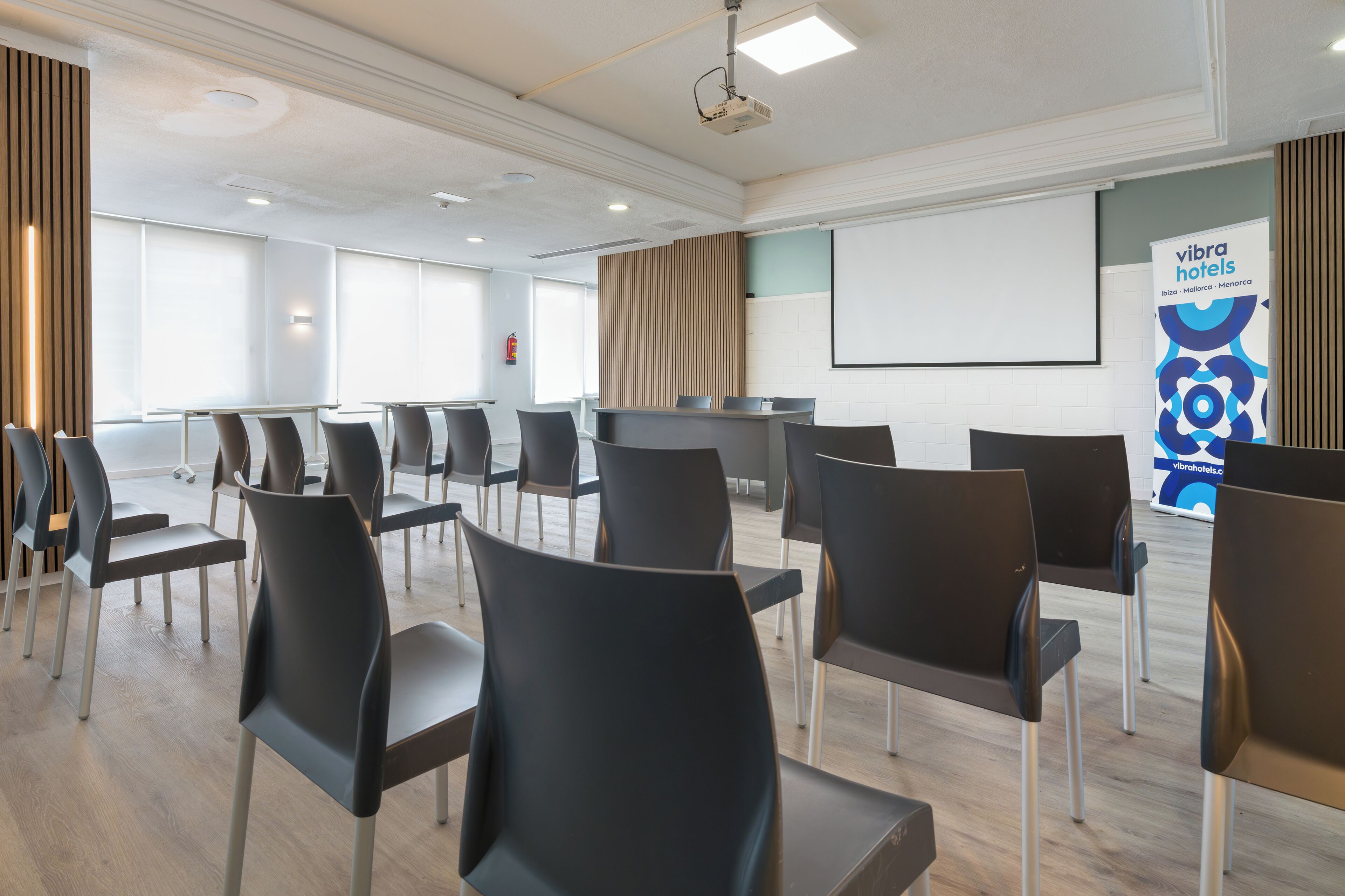 A conference room with rows of chairs, a projector screen, and a banner for vibra hotels.
