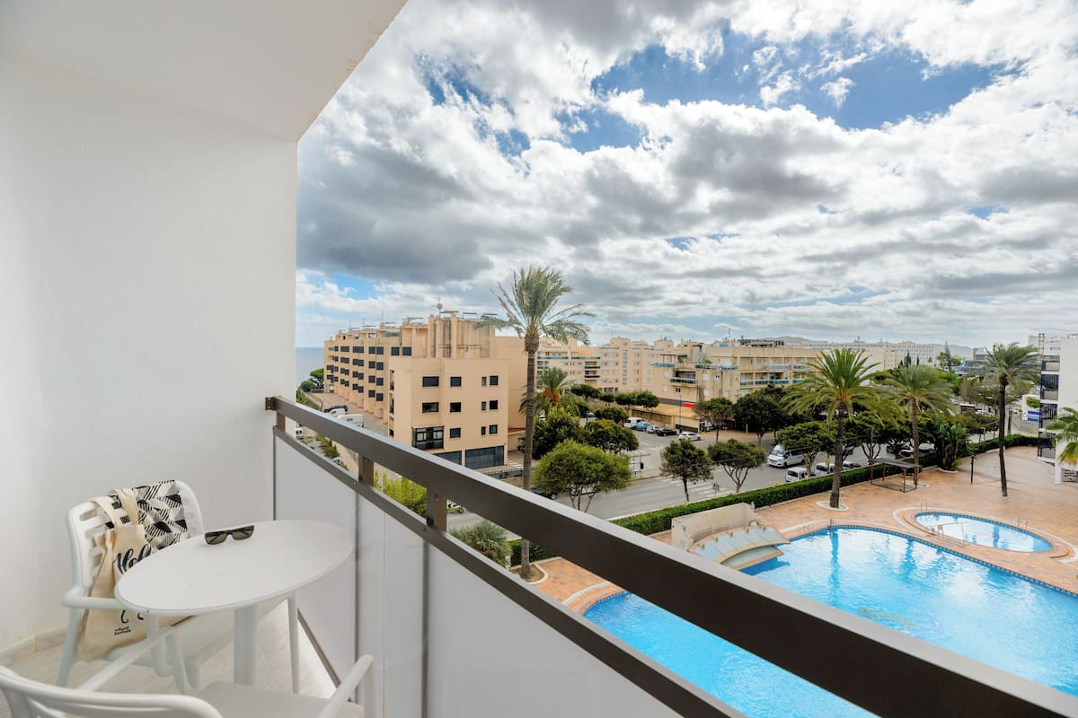 Un balcón con vista a una piscina, palmeras y edificios circundantes.