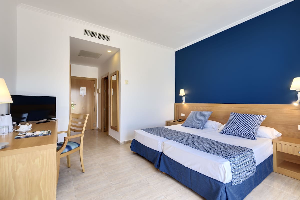 A hotel room with a bed, a desk with a television, and a chair.