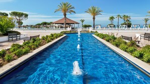 Una piscina con una fuente central, rodeada de bancos y palmeras.
