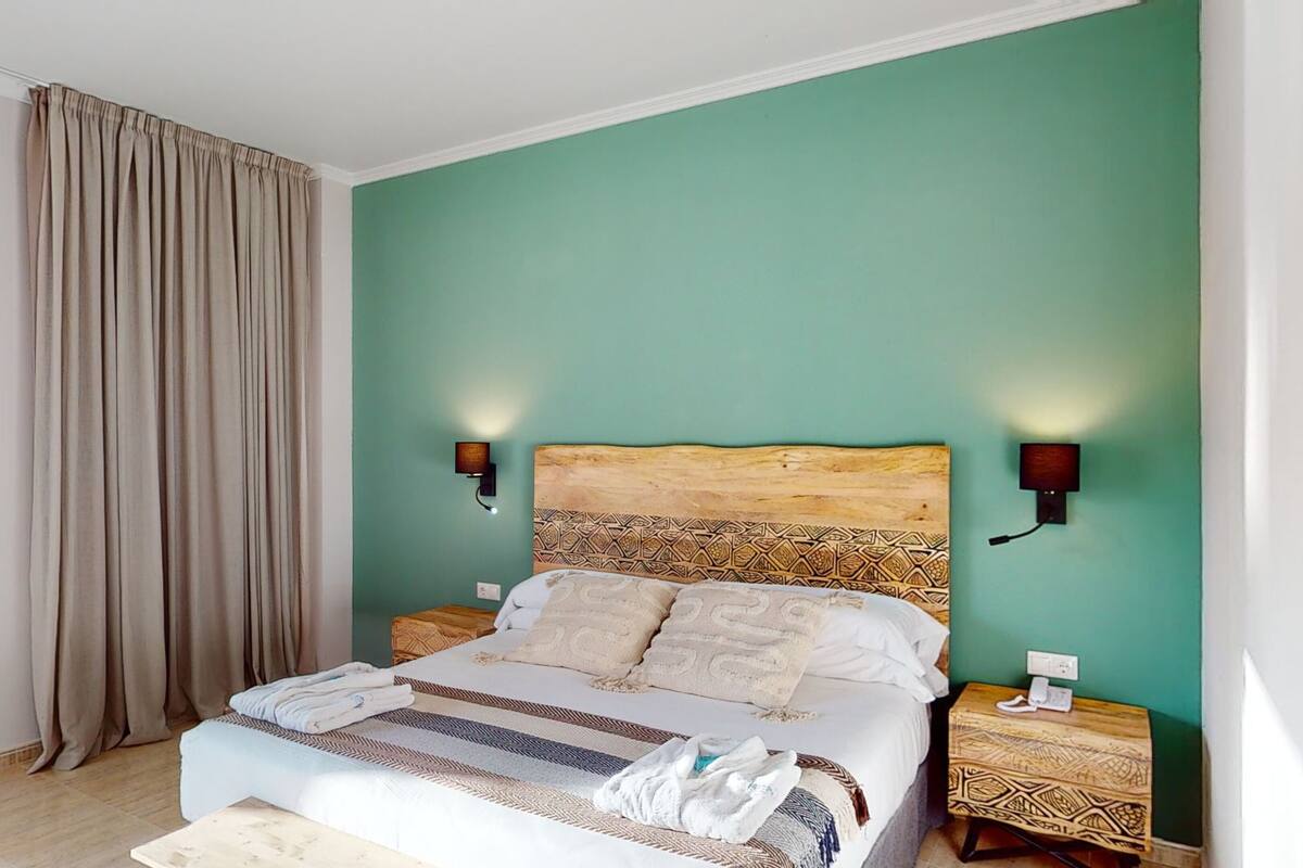A bedroom with a bed, two bedside tables, a nightstand, a lamp, and a curtain.