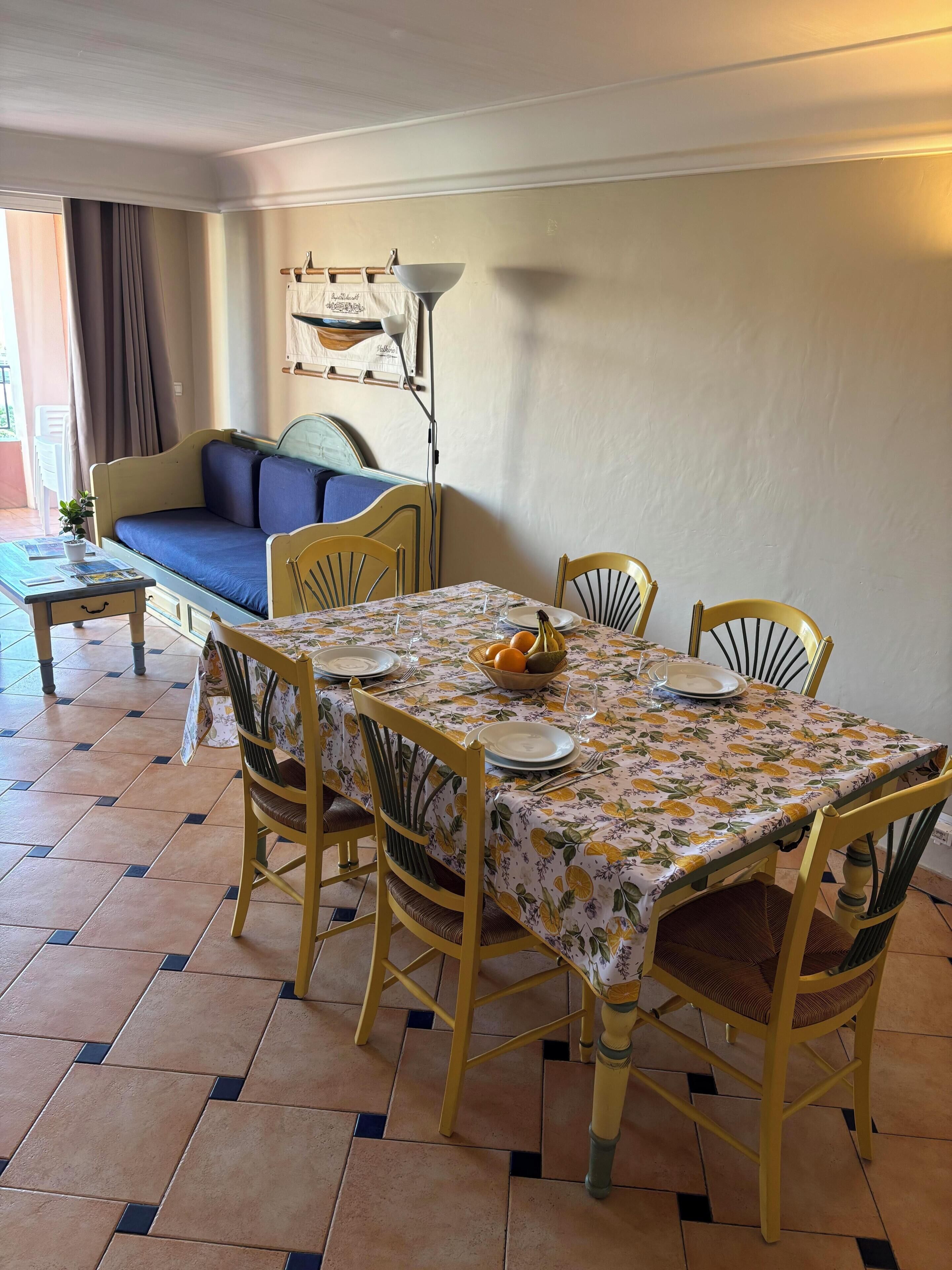 Un coin repas avec une table dressée pour quatre personnes, entouré de chaises jaunes, d’un canapé et d’un lampadaire.