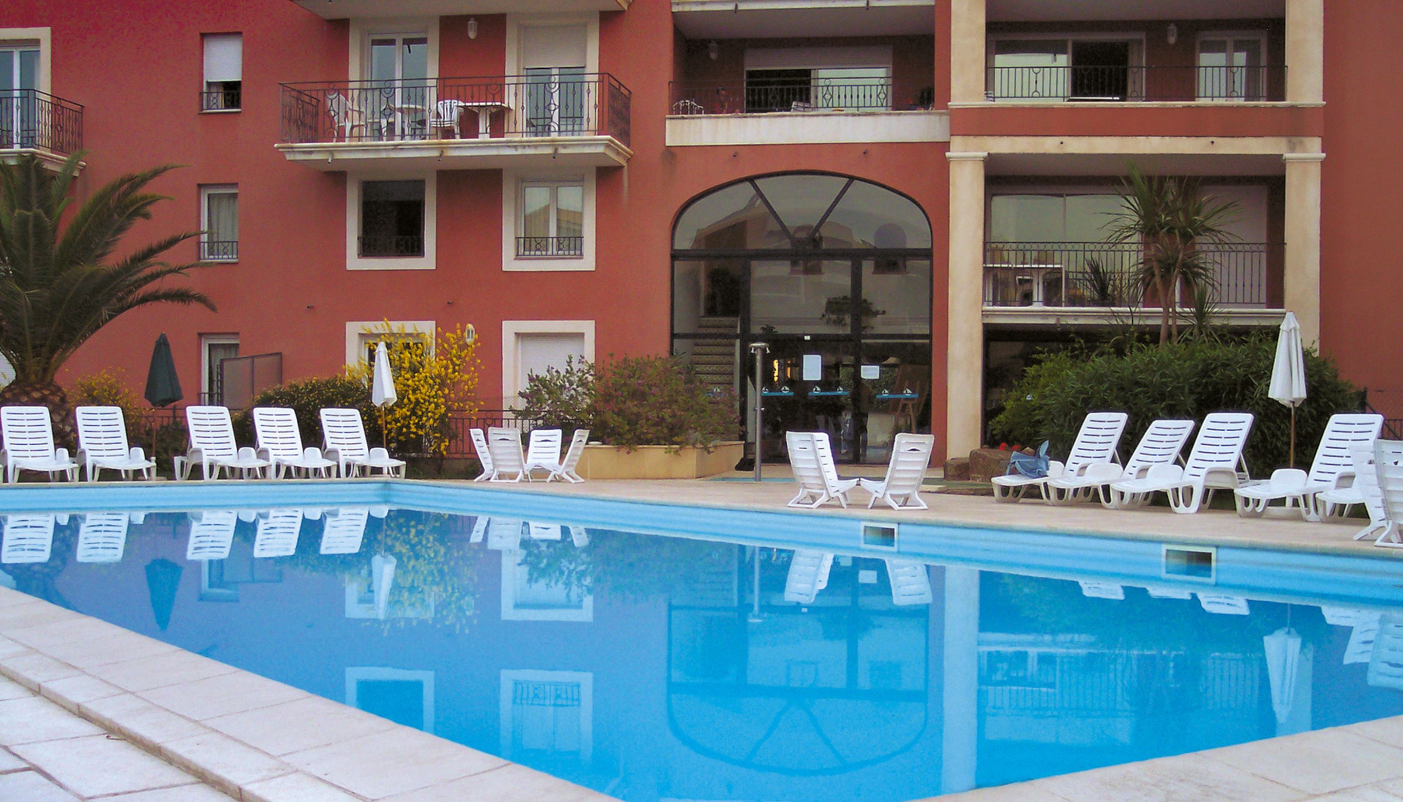 A swimming pool with white lounge chairs and a building with balconies in the background.