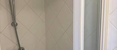 A shower with a handheld showerhead and a fixed showerhead, a corner with decorative tiles, and a glass door leading to a shower area.