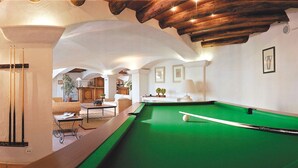 A pool table with a green felt surface, a pool cue, and a white cue ball. There are two framed pictures on the wall, a lamp, and a potted plant. - Lagrange Vacances Port Marine (Sainte-Maxime)