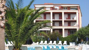 A hotel with a pool area, lounge chairs, and a palm tree. - Lagrange Vacances Port Marine (Sainte-Maxime)