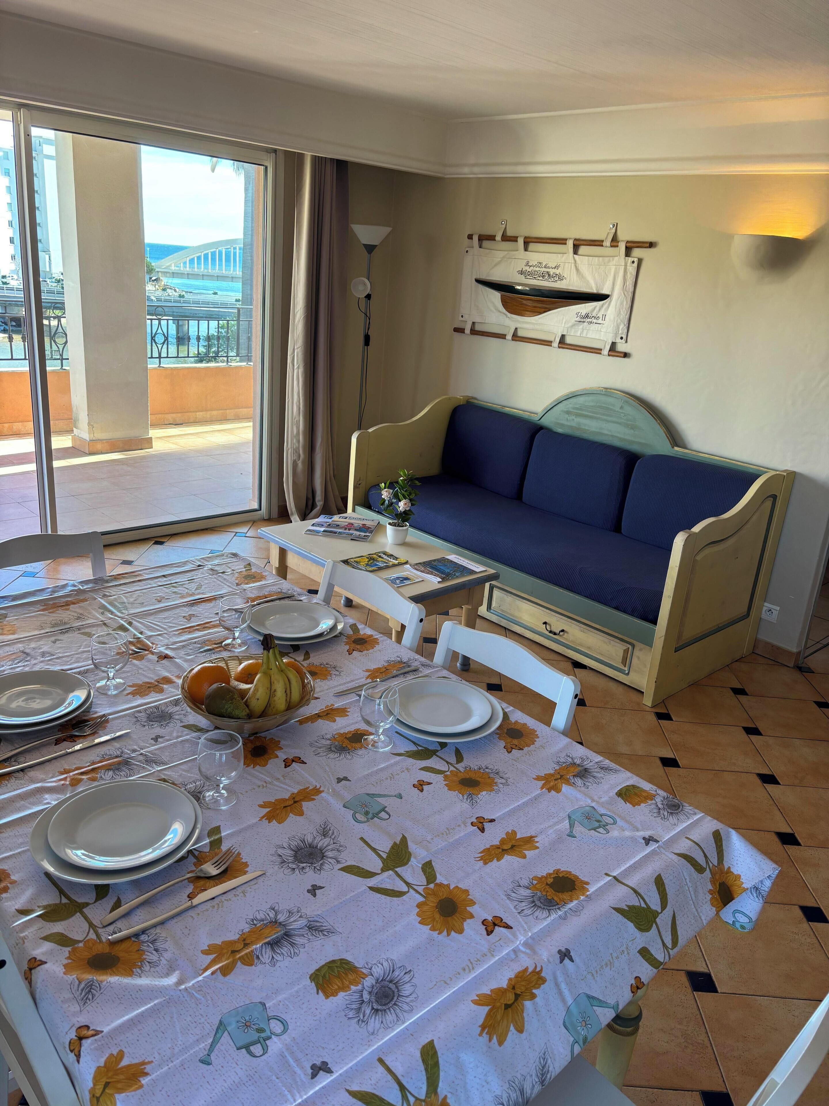 A dining area with a table set for two, a sofa, and a balcony view.