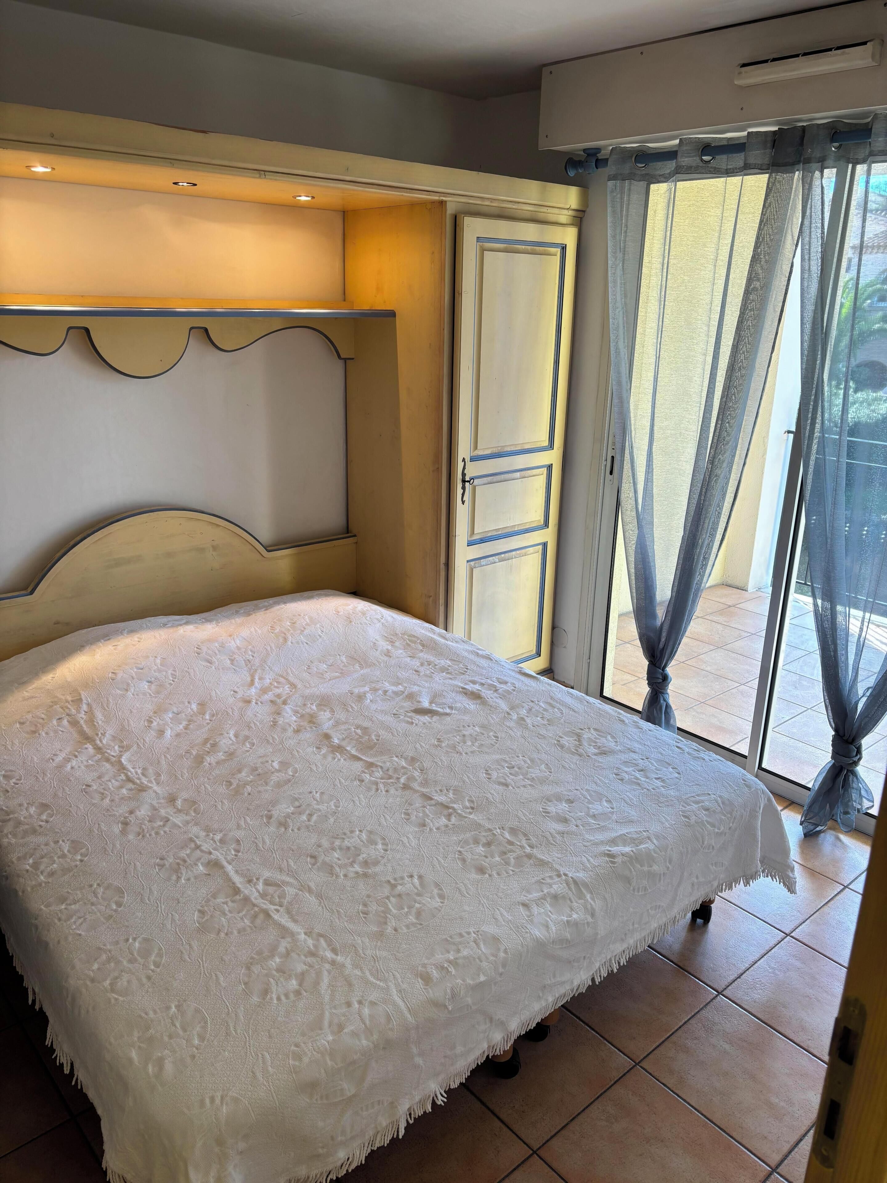 A bed with a white bedspread, a wooden headboard, and a window with curtains.
