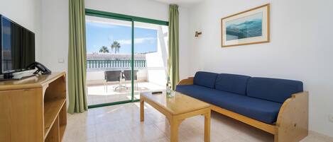 A room with a blue sofa, wooden coffee table, and a TV on a wooden stand.