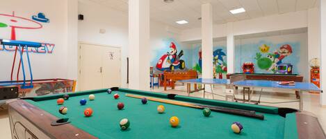 Una mesa de billar con billas, una mesa de ping pong y murales con temática de Mario en las paredes.
