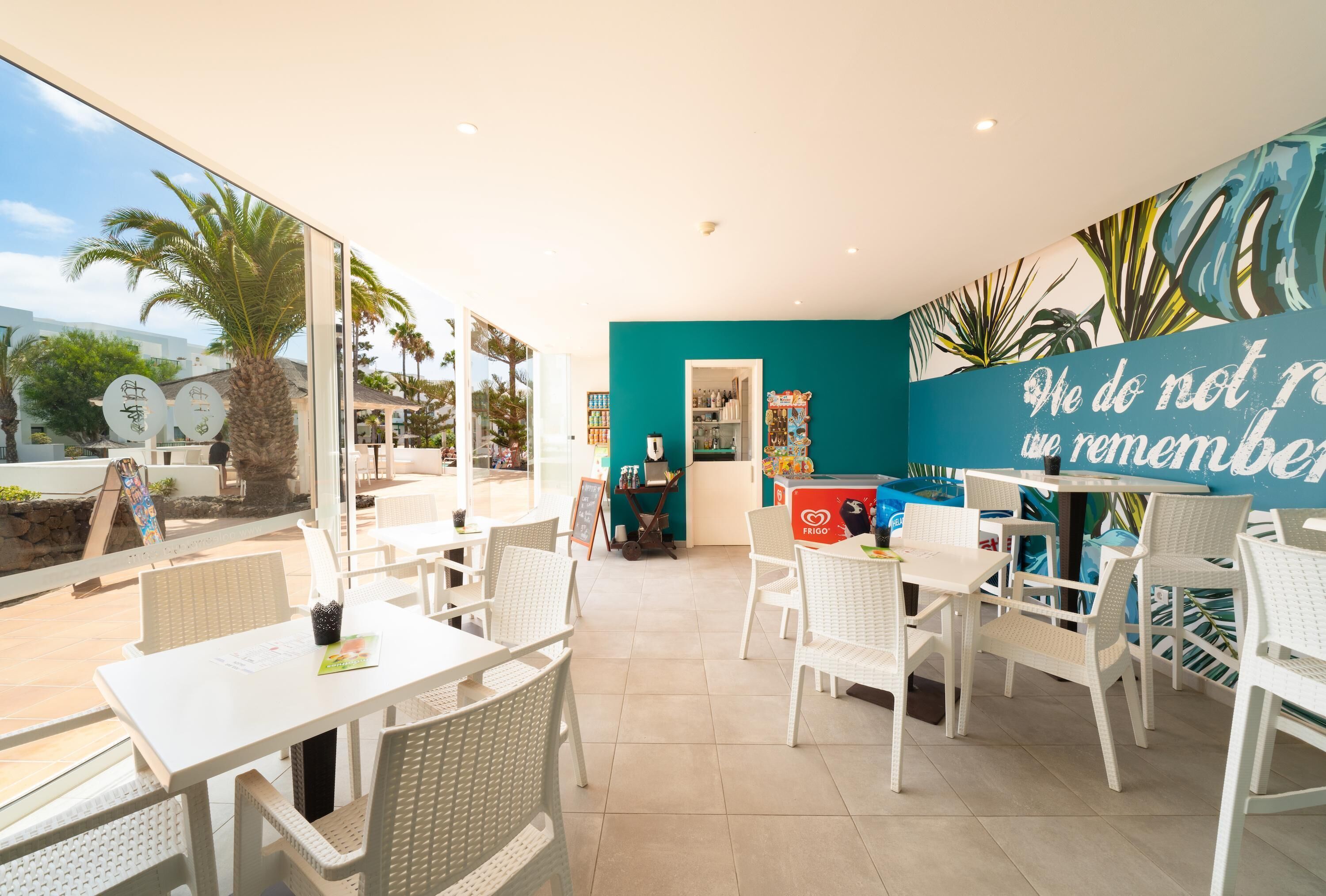 Una cafetería con mobiliario blanco, una pared de acento color turquesa y vistas a la calle.
