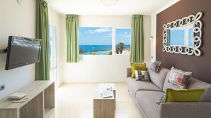 Una sala de estar con televisor, sofá, mesa de centro y vista al mar.