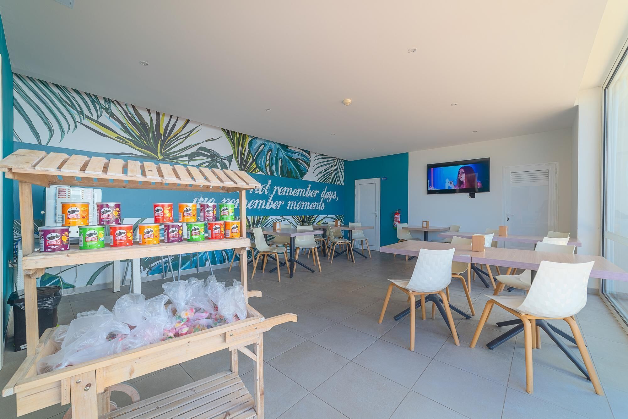A modern dining area with a wall mural, a TV, and a snack cart with Pringles cans.