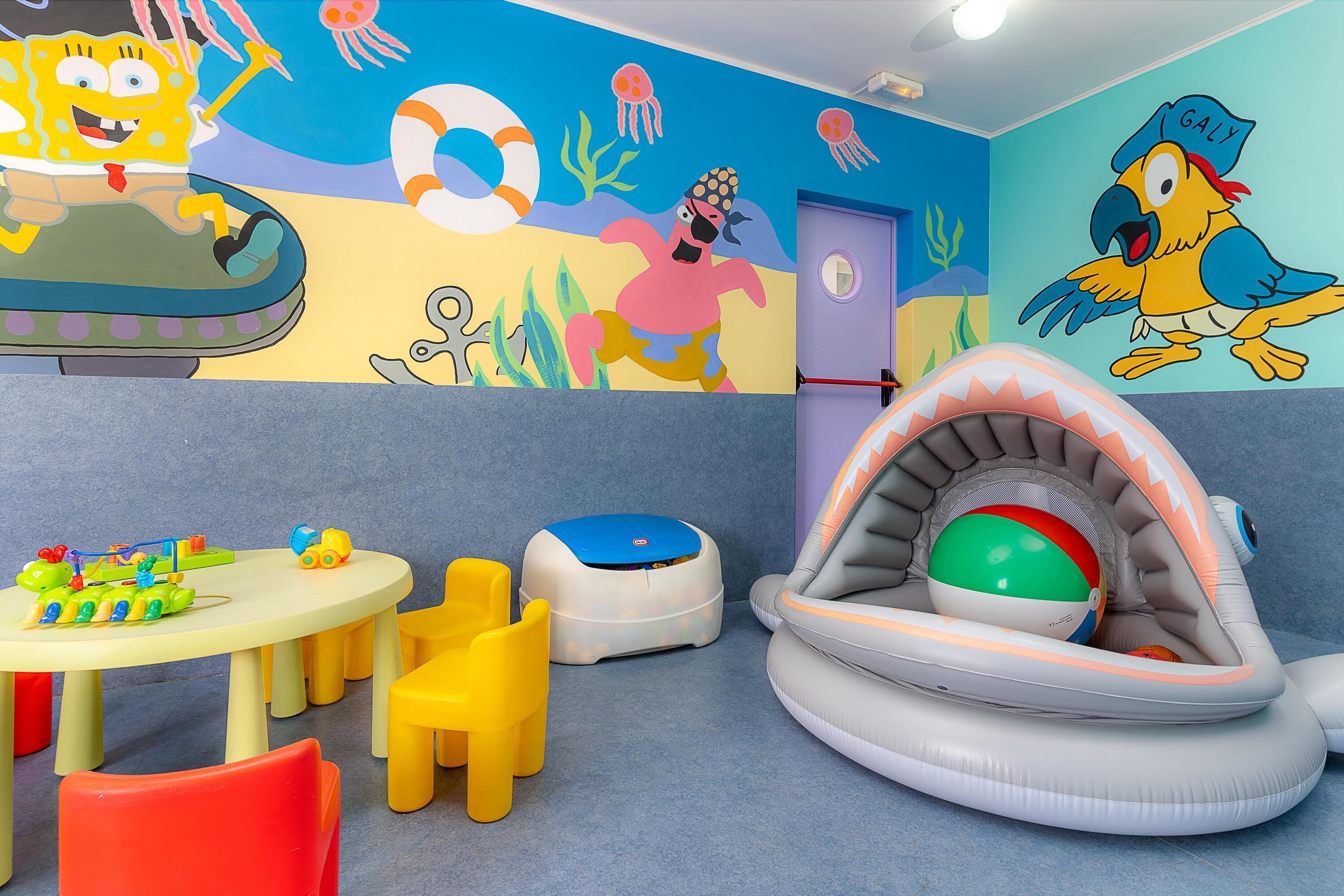 A children's play area with a beach-themed mural, inflatable play structures, and colorful seating.