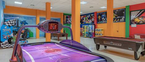A brightly lit indoor arcade with a pinball machine, a Mario Kart game, and various colorful wall decorations.