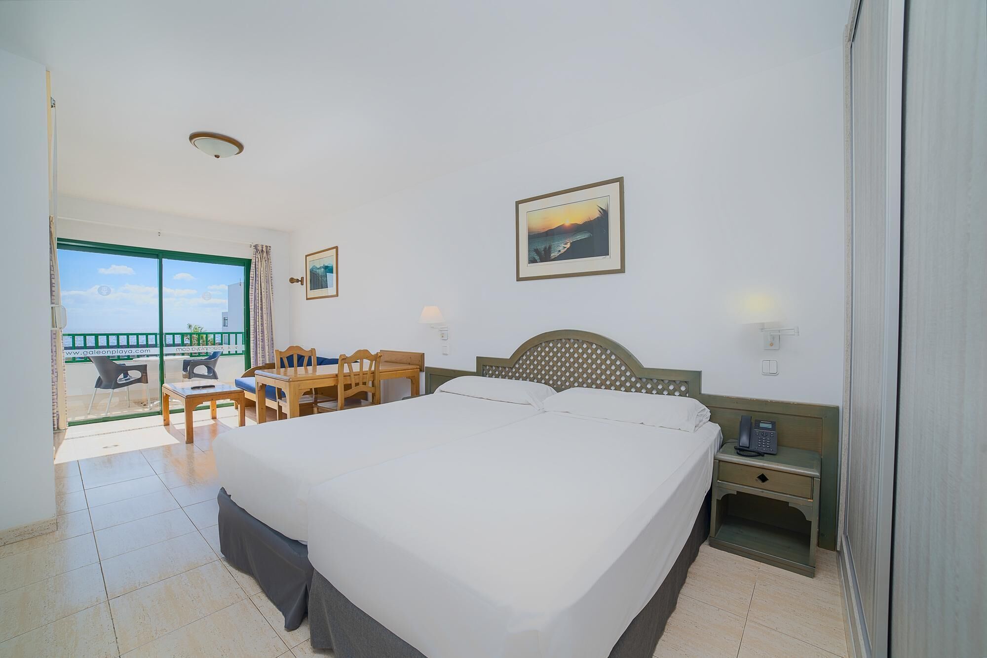 Una camera d'albergo con un letto, una scrivania, una sedia, un telefono e un quadro appeso al muro.