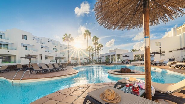 Un área de piscina con sillones de descanso y sombrillas, rodeada de edificios modernos.