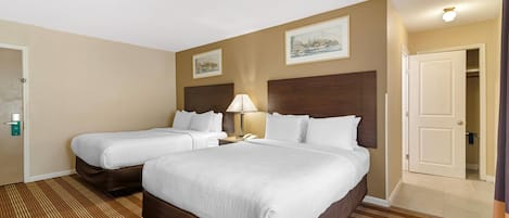 A hotel room with two beds, a desk, a chair, a lamp, and a door leading to a closet.