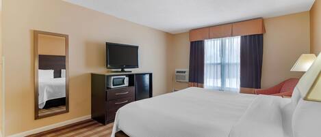 Habitación de hotel con una cama grande, un televisor en una cómoda, un espejo, una ventana con cortinas y una lámpara.