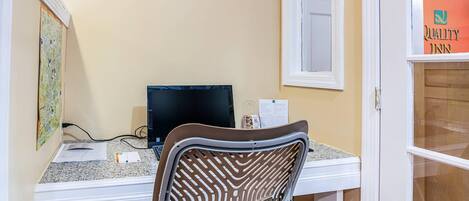 A room with a desk, a chair, a computer, and a window with a sign reading "Quality Inn".