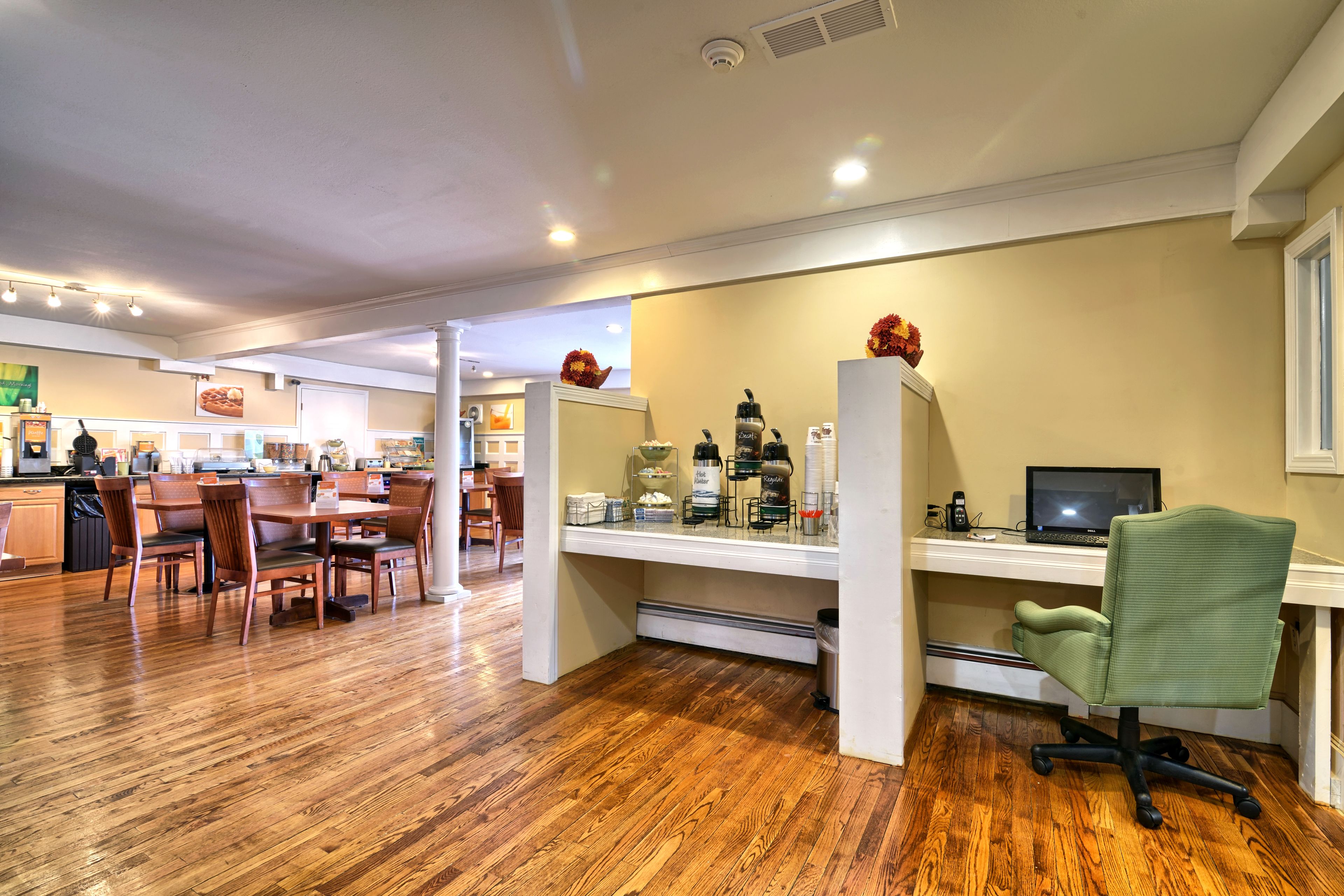 A modern kitchen with wooden flooring, a dining area with chairs, and a workspace with a computer and office chair.