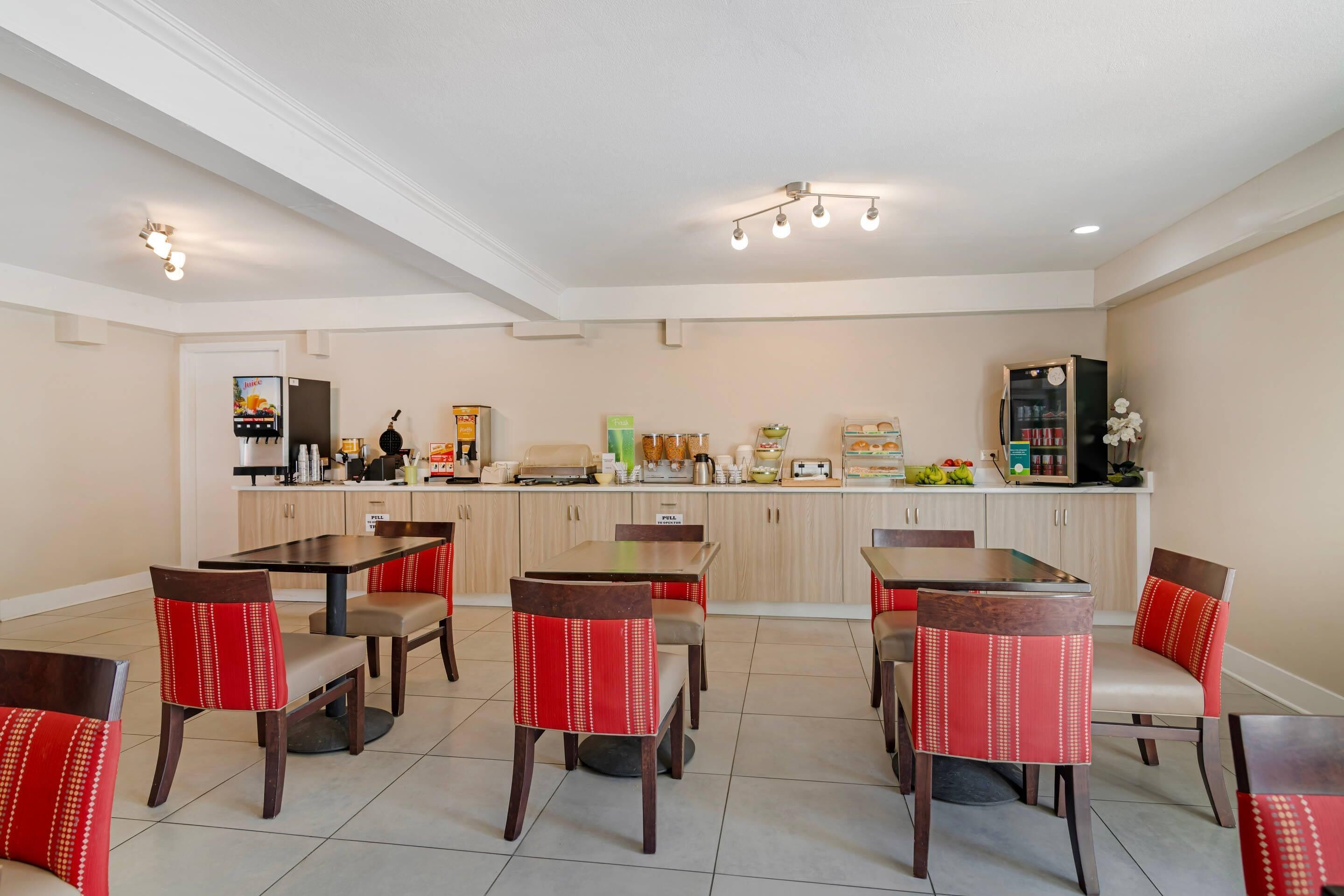 A dining area with multiple tables and chairs, a kitchen in the background, and a ceiling with recessed lighting.