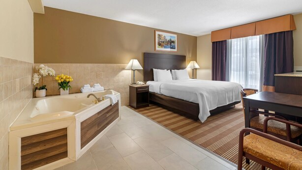 Habitación de hotel con una cama grande, un baño independiente con bañera, un escritorio con silla y una ventana con cortinas.