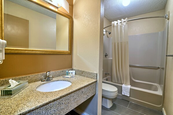 A bathroom with a granite countertop sink, a mirror, a toilet, and a bathtub with a shower curtain.