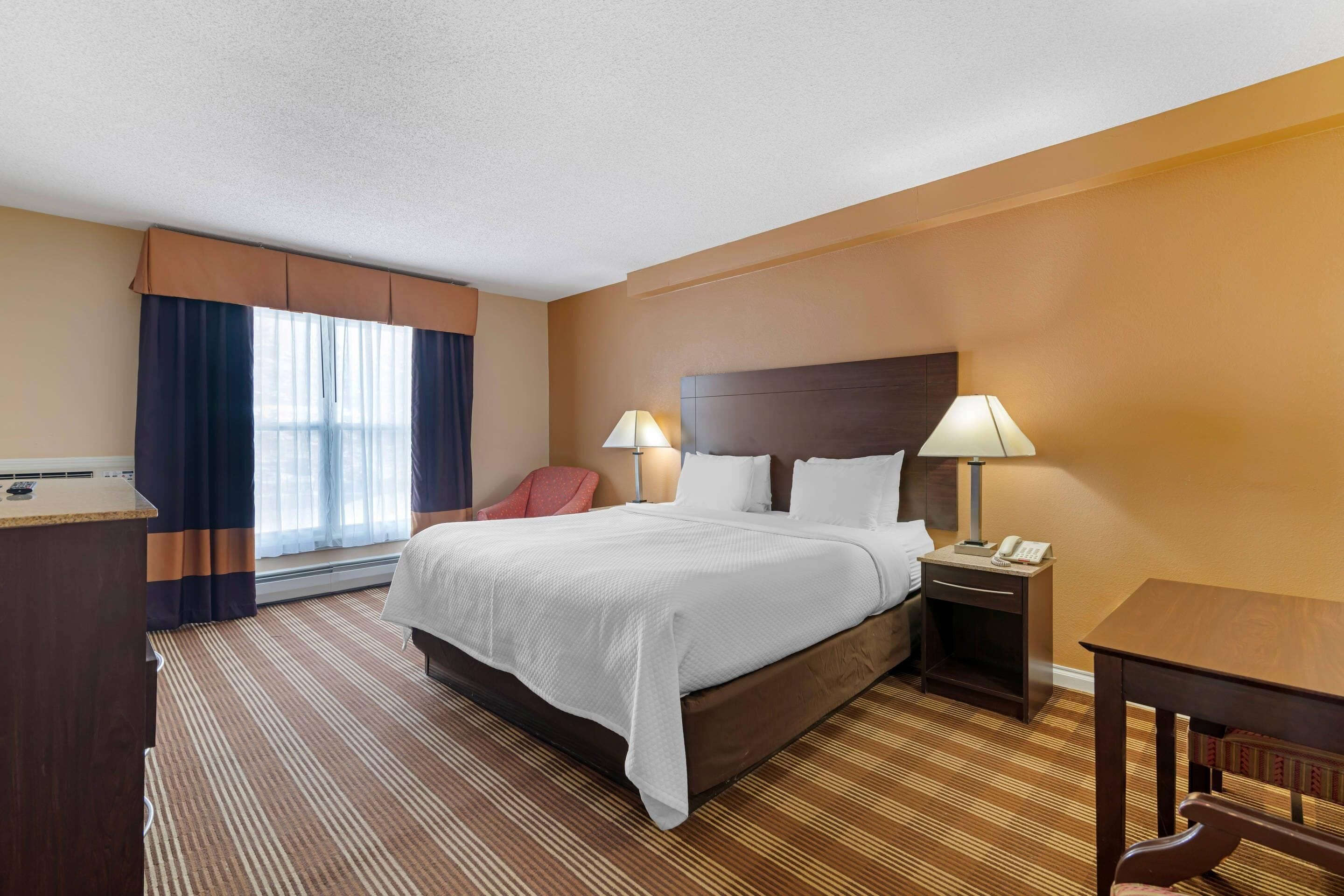 A hotel room with a large bed, two bedside lamps, a desk, and a chair.