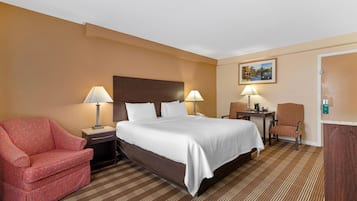 Una habitación de hotel con una cama grande, dos mesitas de noche con lámparas, un sillón rojo y una pequeña mesa con una silla.