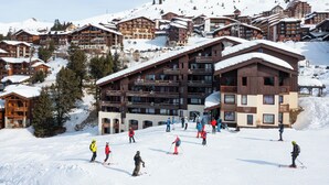 A ski resort with multiple wooden buildings, ski slopes, and skiers. - Pierre & Vacances Residence Le Quartz (La Plagne-Tarentaise)