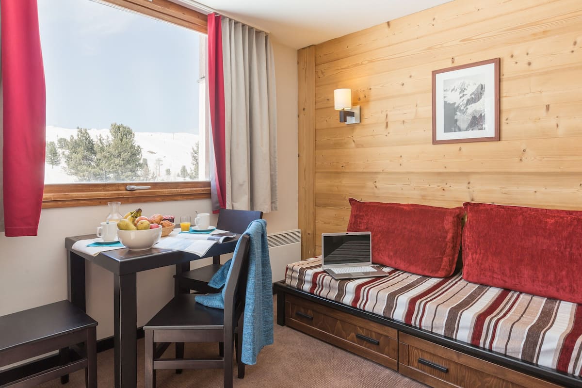 Une pièce chaleureuse avec un mur en bois, un lit avec des oreillers rouges, un bureau avec un ordinateur portable et une fenêtre avec des rideaux.