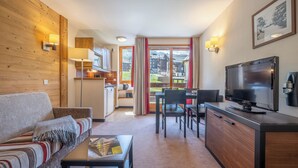 A modern living room with a sofa, coffee table, TV, and a dining area with chairs and a table. - Pierre & Vacances Residence Le Quartz (La Plagne-Tarentaise)