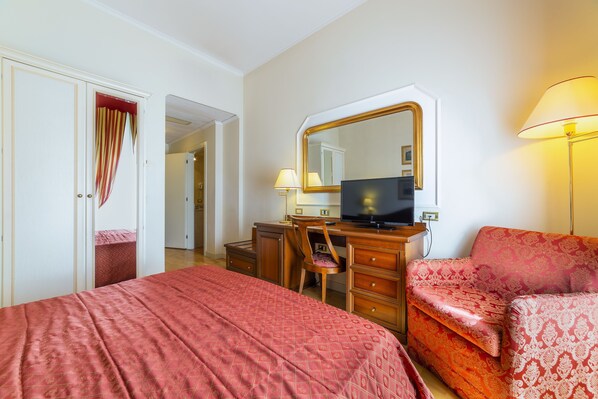 Habitación de hotel con cama, escritorio, silla, televisor y lámpara.