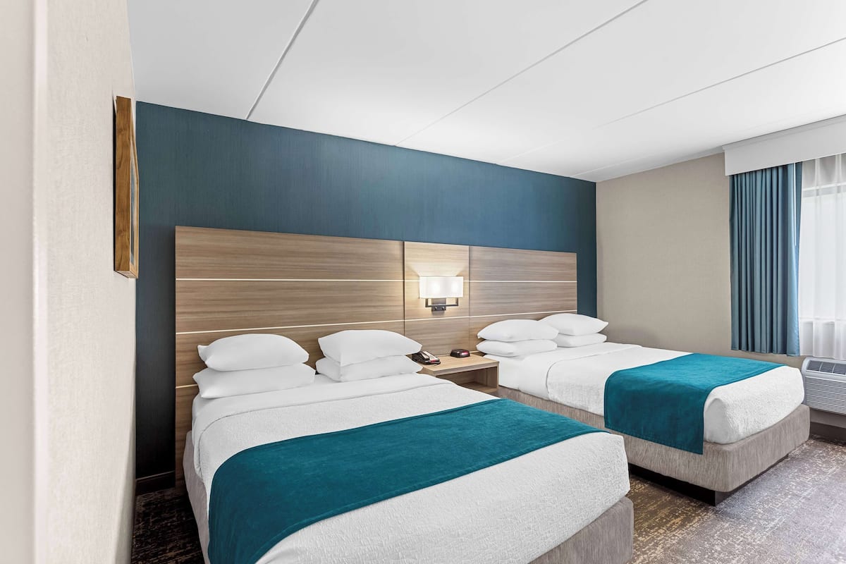 Habitación de hotel con dos camas, una mesita de noche con lámpara y una ventana con cortinas.