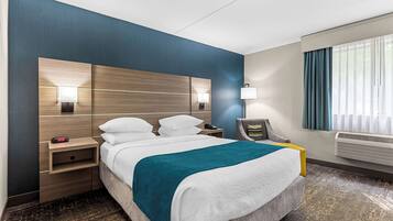 Een hotelkamer met een groot bed, bedlampen, een nachtkastje, een stoel en een raam met gordijnen.