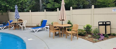 A poolside area with lounge chairs, a table, and umbrellas.