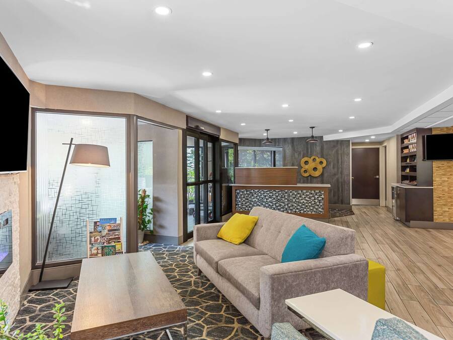 A modern hotel lobby with a stone-patterned floor, a sofa with colorful cushions, a wooden coffee table, and a large lamp.