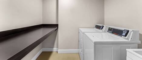 A laundry room with a dark brown counter, two stacked washing machines, and a ceiling light.