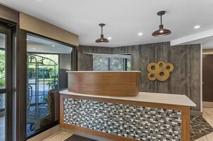 Un mostrador de recepción con cubierta de madera y base de mosaicos, un ventanal grande y un adorno colgado en la pared.