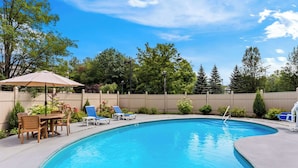 A swimming pool with a wooden deck, lounge chairs, and a table with chairs. - Best Western West Lebanon-Hanover Hotel (West Lebanon)