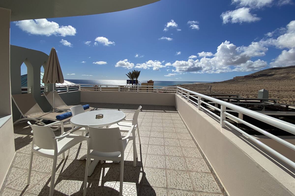 Une terrasse avec une table et des chaises, une vue sur la mer et un paysage montagneux.