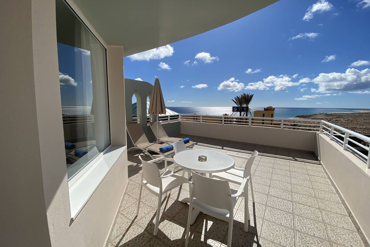 Un balcon avec une table et des chaises, une vue sur la mer et un palmier.