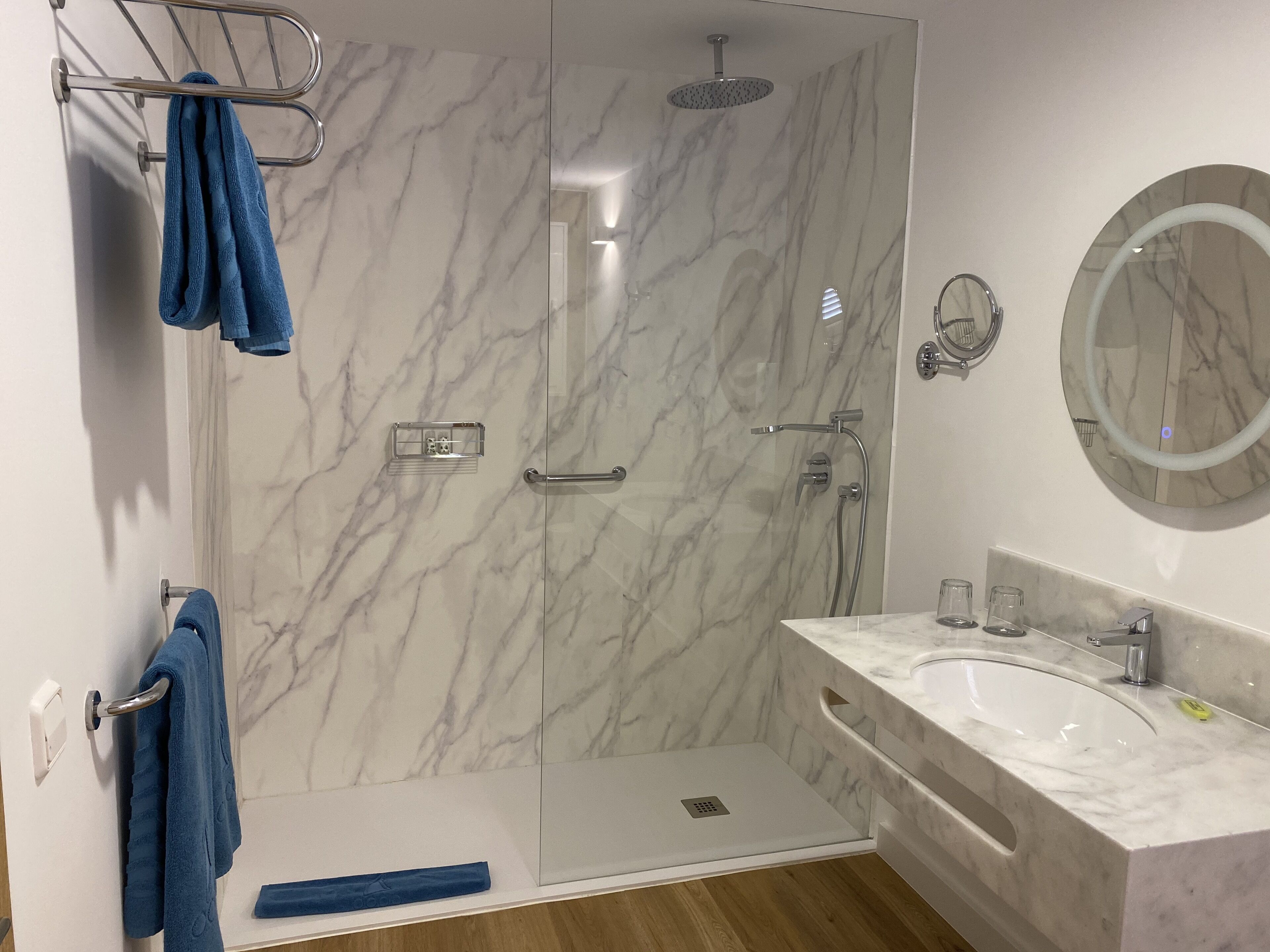 A modern bathroom with a marble shower enclosure, a glass shower door, a vanity with a sink, and a mirror.