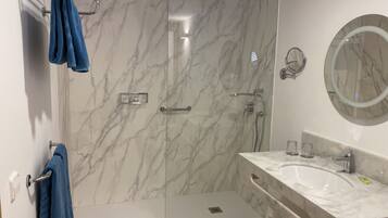 A modern bathroom with a marble shower enclosure, a glass shower door, a vanity with a sink, and a mirror.