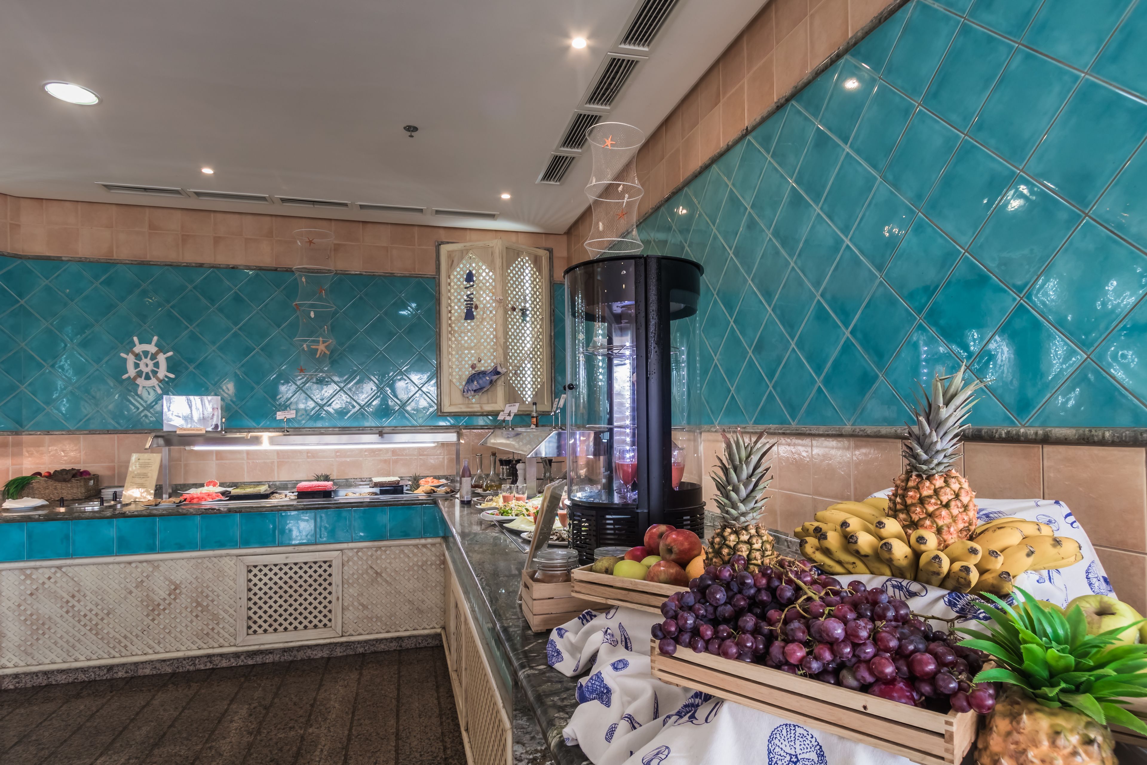 A buffet area with a variety of fruits and a decorative wall with a ship wheel design.