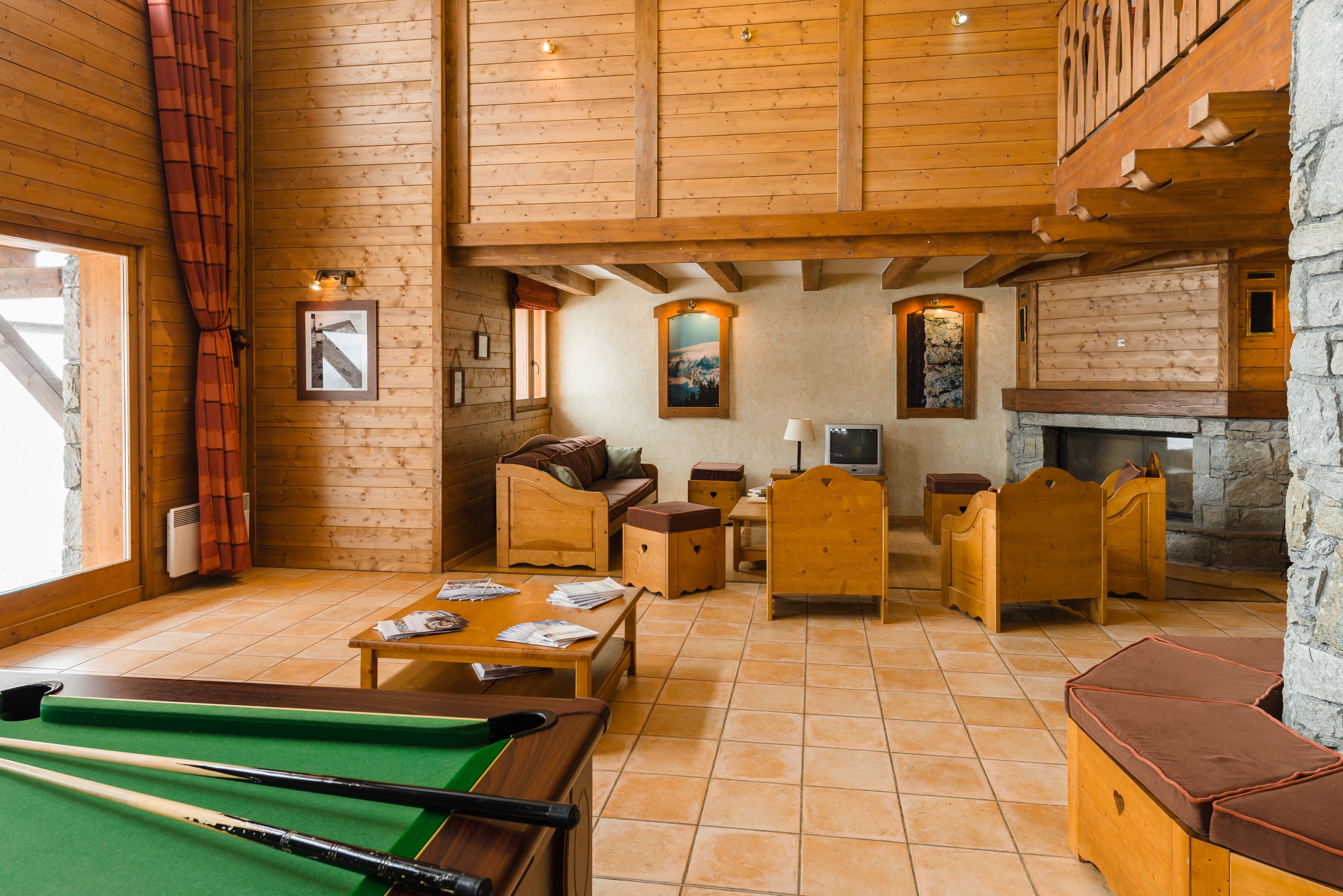 A cozy room with a pool table, wooden furniture, and a stone fireplace.