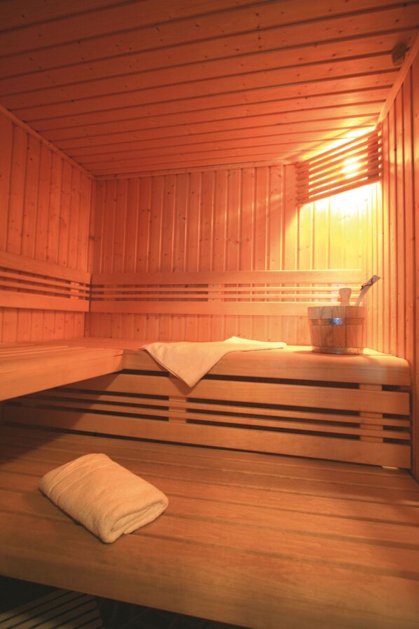 Eine Sauna mit Holzwänden und -bänken, ein Handtuch auf dem Boden und ein Eimer auf der Bank.